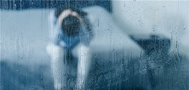 Frau in Hocke hinter einer verregneten Scheibe.