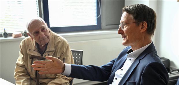 Karl Lauterbach erklärt einem älteren Patienten etwas Technisches.