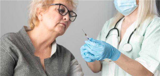 Eine Ärztin zieht eine Impfung auf, eine ältere Frau sieht sich die Spritze an.