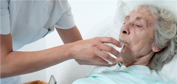 Pflegerin gibt älterer Dame zu trinken.