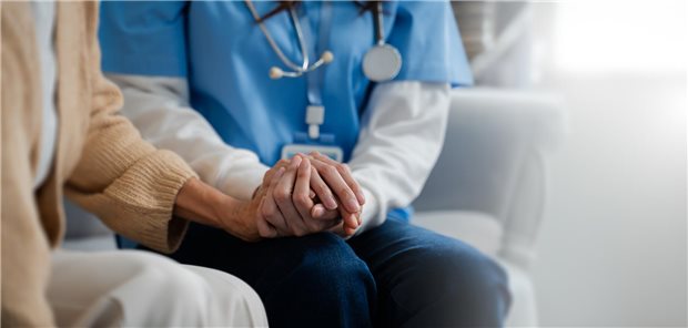 Eine Person mit Sthetotskop um den Hals hält die Hand einer Patientin.