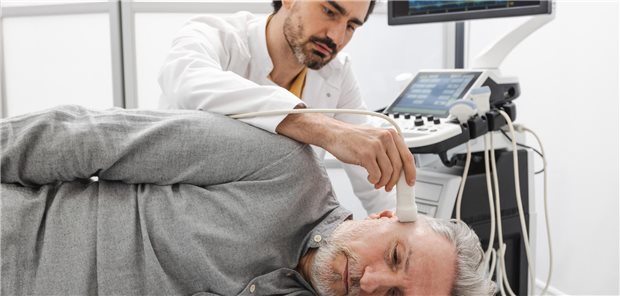 Ein Ultraschalltechniker untersucht die Aa. temporales und axillares eines Mannes, indem er den Ultraschallkopf an die Schläfe des Patienten ansetzt.