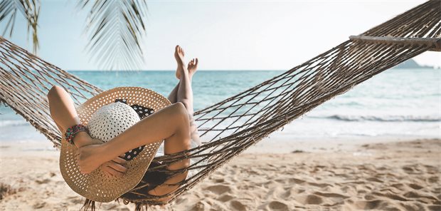 Eine Frau liegt entspannt vor dem Meer in einer Hängematte.