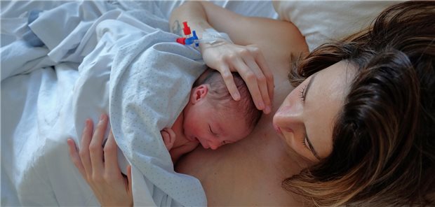 Ein neugeborenes Baby liegt Haut an Haut auf dem Oberkörper seiner Mutter.