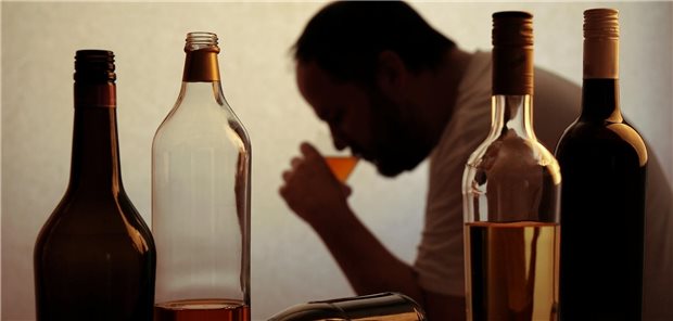 Ein Mann im Hintergrund nimmt einen Schluck von einem Drink. Im Vordergrund stehen vier Flaschen mit alkoholischen Getränken.