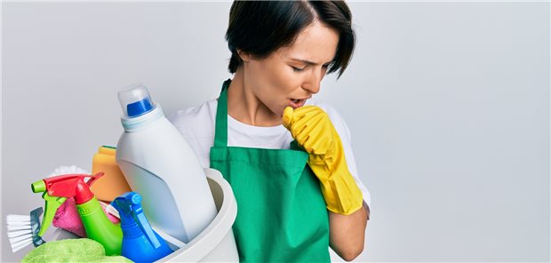 Junge Frau hustet, während sie Putzmittel auf der Hüfte balanciert.