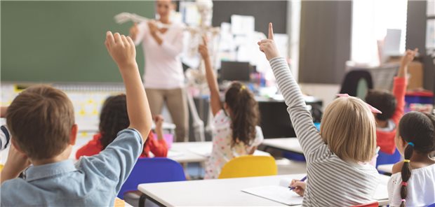 Schüler heben die Hände, während die Lehrerin im Klassenzimmer die Funktionsweise des menschlichen Skeletts erklärt.