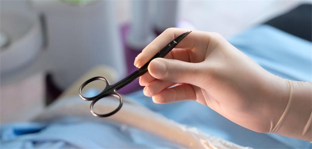 Hände eines Arzthelfers in Schutzhandschuhen mit einem Instrument bei der Behandlung eines Patienten.