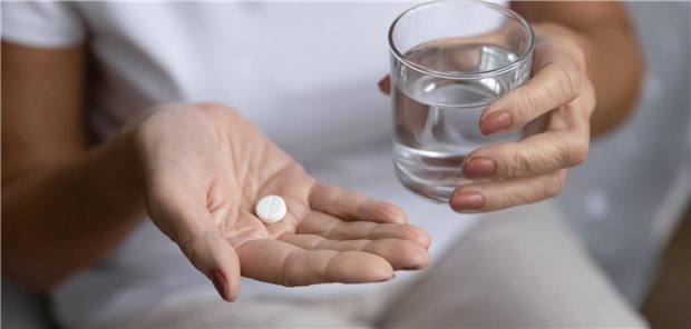 Nahaufnahme einer älteren Frau, die eine Tablette und ein Glas Wasser in der Hand hält.