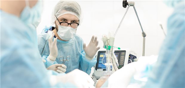 Chirurg im OP schaut angestrengt nach vorne und hält seine Hände hoch.