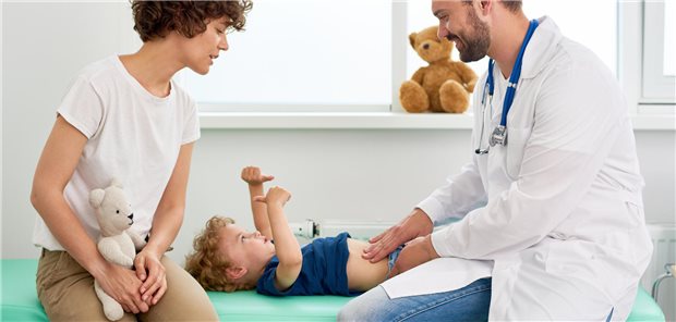 Porträt eines lächelnden Arztes, der den Bauch eines kleinen Jungen untersucht und ihn auffordert zu sagen, wo es weh tut.