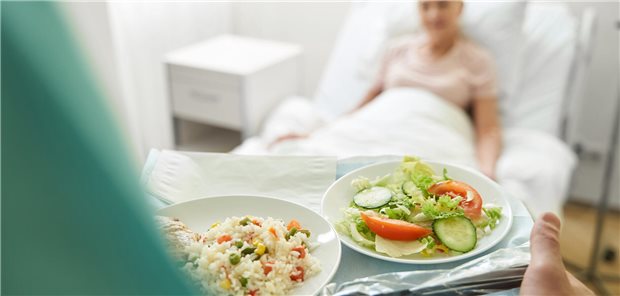 Ein medizinischer Angestellter bringt ein Tablett mit zwei Tellern voller Essen zu einer Patientin.