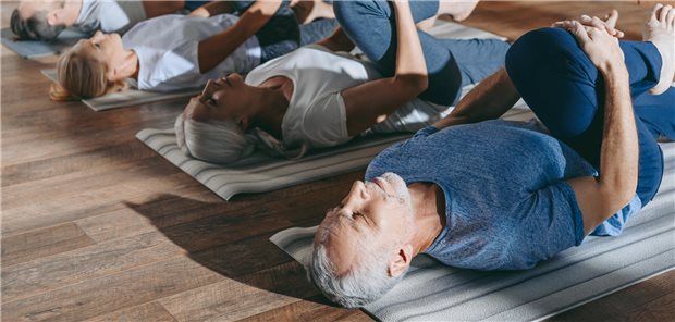 Eine Gruppe von Menschen, die sich auf Yogamatten in einem Sportstudio dehnen.