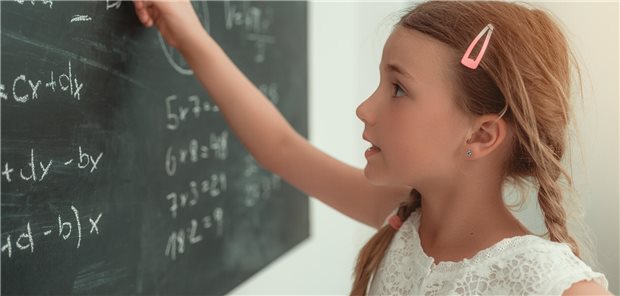 Junges Mädchen das an einer Tafel steht und Rechenaufgaben löst.