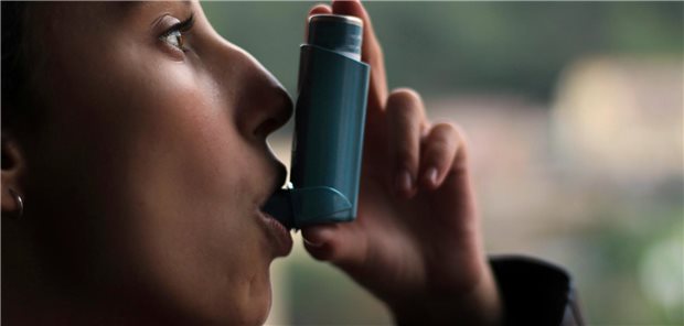 Ein junges Mädchen benutzt einen blauen Inhalator, der eine Kartusche mit einem inhalativen Kortikosteroide trägt, um einen Asthmaanfall zu verhindern.