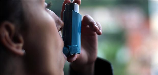 Junge Frau, die einen blauen Asthma-Inhalator benutzt.
