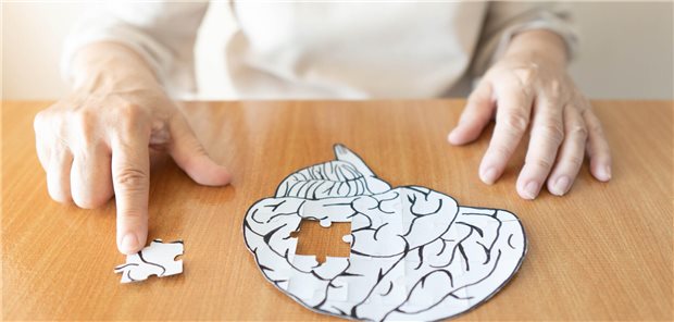 Ältere Frau hat ein Gehirnmodell aus Papier vor sich liegen, in dem ein Puzzleteil fehlt.