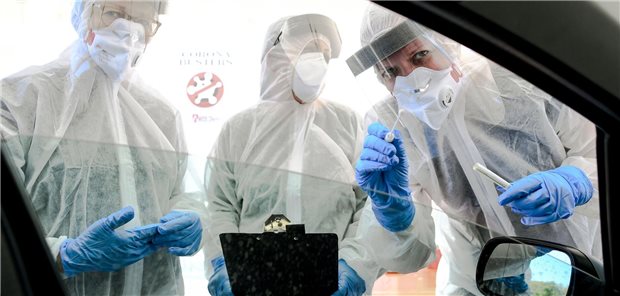 Mitarbeiter vom Gesundheitsamt halten ein Abstrichstäbchen in ein Autofenster in der ambulanten Corona-Test- Einrichtung.