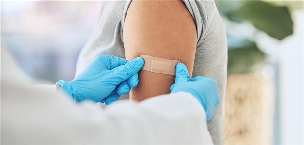Ein Arzt platziert das Pflaster über Einstichstelle der Impfung auf dem Arm eines Patienten.