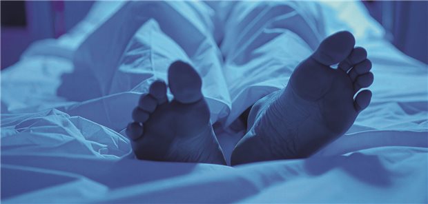 Die Füße einer Leiche auf einem Bett, die Beine zugedeckt mit weißem Tuch.