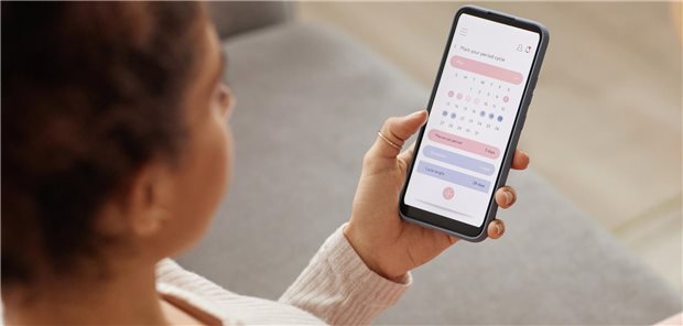 Nahaufnahme einer jungen Frau, die ein Smartphone in der Hand hält auf dem eine Periodentracker-App geöffnet ist.