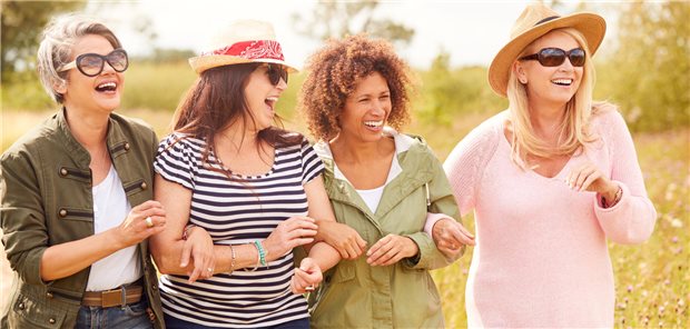 Vier mittelalte Frauen laufen gemeinsam über eine Wiese und lachen.