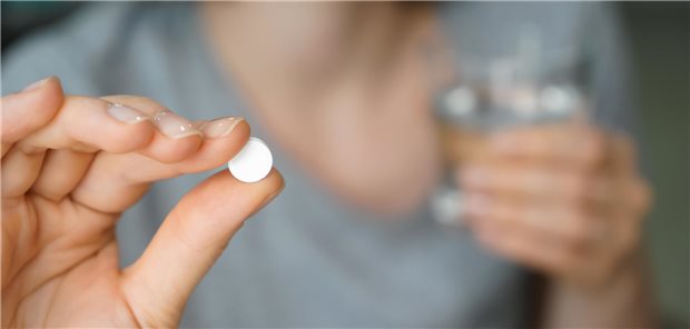 Nahaufnahme der Hand einer Frau die eine runde weiße Tablette zwischen Daumen und Zeigefinger hält.