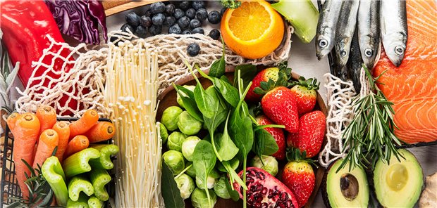 Viele verschiedene Lebensmittel auf einem Tisch: Karotten, Sellerie, Rosenkohl, Erdbeeren, Avocado, Oilze, Blaubeeren, Paprika und weiteres. 