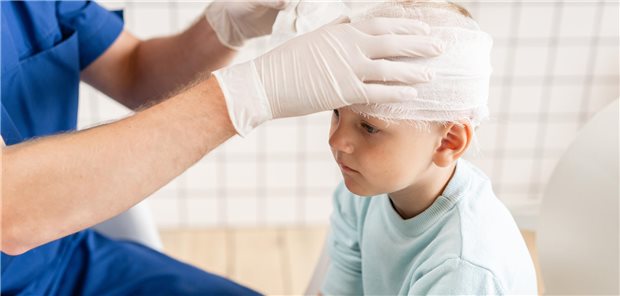Ein Arzt legt einem Kind im Krankenhaus einen Verband am Kopf an.