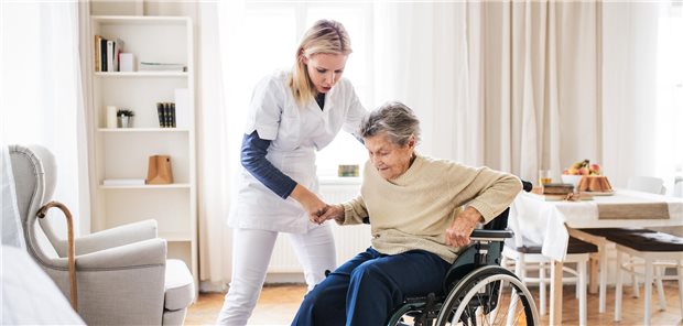 Eine Pflegekraft hilft einer Frau beim Aufstehen aus einem Rollstuhl.