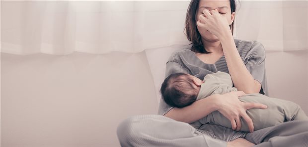 Frau mit Säugling im Arm, die Augen geschlossen, die Daumen und Zeigefinger auf dem Nasenrücken.