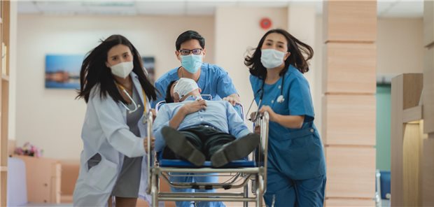 Medizin und Pflege: Es lebe die Teamarbeit Ärztin und Pflegekräfte schieben einen Patienten durch einen Krankenhausflur.