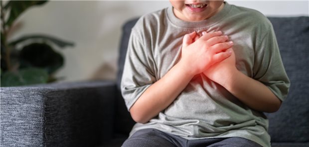 Thoraxschmerzen bei Kindern haben laut Analyse selten kardiale Ursachen Nahaufnahme des Oberkörpers eines Jungen, der sich aufgrund von Brustschmerzen, mit beiden Händen an die Brust fasst.