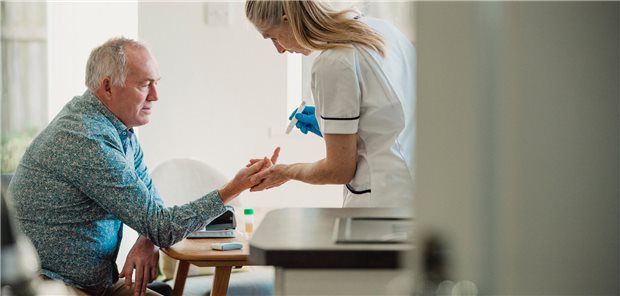 Ein älterer Diabetiker lässt zu Hause von einer Gemeindeschwester seinen Blutzuckerspiegel überprüfen.
