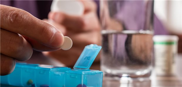 Nahaufnahme einer männliche Hand, die die Tagesdosen an Vitaminen, Medikamenten, Tabletten und Nahrungsergänzungsmitteln in eine Tablettenbox füllt.