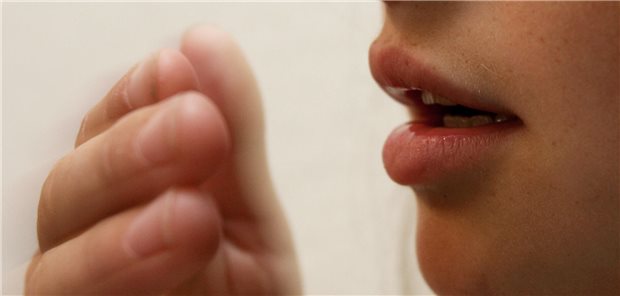 Aufnahme eines Teenager-Mädchens das hustet. Der Ausschnitt ist so gewählt, dass man nur den Mund und eine Hand vor dem Mund sehen kann.