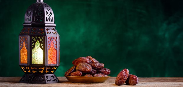 Datteln in einer Schale zum Fastenbrechen und eine Ramadan Laterne auf einem Holztisch.