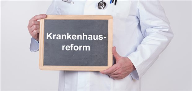 Ein Arzt hält eine Tafel auf der Krankenhausreform steht in seinen Händen.