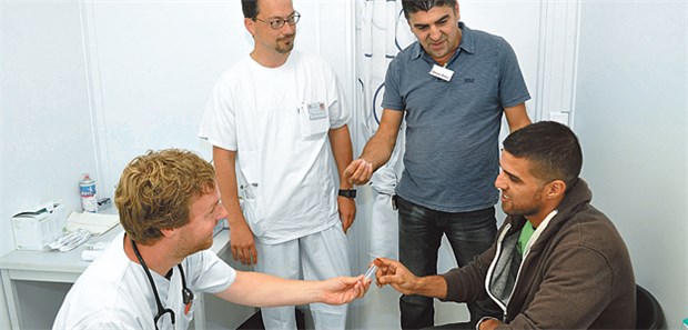 BÄK fordert Regelversorgung für Flüchtlinge Dr. Alexander Humberg (l.) und Dr. Florian Reifferscheid vom Uniklinikum Schleswig-Holstein versorgen in der neuen Flüchtlingsunterkunft in Rendsburg mit Hilfe von Dolmetscher Sirwan Baban einen Patienten aus dem Irak.