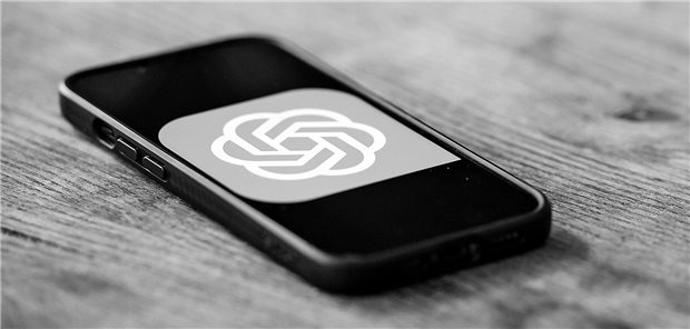 Ein Handy mit dem ChatGPT-Logo liegt auf einem Holztisch.