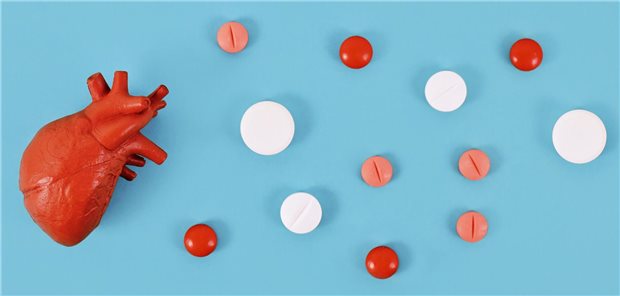 Ein Herz-Modell und mehrere Tabletten liegen auf blauem Hintergrund