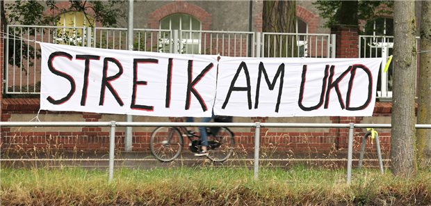 Tarif-Eckpunkte für NRW-Unikliniken vereinbart Ein Banner mit der Aufschrift „Streik Am UKD“ hängt vor der Uniklinik Düsseldorf. Die Beschäftigten der Unikliniken in Nordrhein-Westfalen fordern seit Monaten einen Entlastungs-Tarifvertrag. Nun scheint die Einigung da.