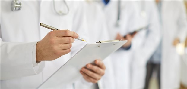 Ein Arzt der sich Notizen zur Einschätzung des Gesundheitszustandes der Patientin auf den Unterlagen auf seinem Klemmbrett macht.