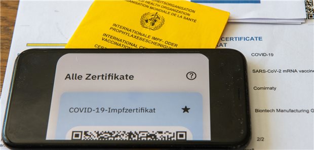 Mit falschem Corona-Impfpass in die Apotheke: Kunde bleibt ohne Strafe Ein Impfpass und ein Smartphone, auf dem die App CovPass läuft, liegen auf einem Impfzertifikat.