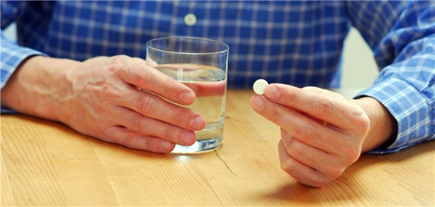 Eine Hand, die eine Tablette hält und eine Hand mit Wasserglas