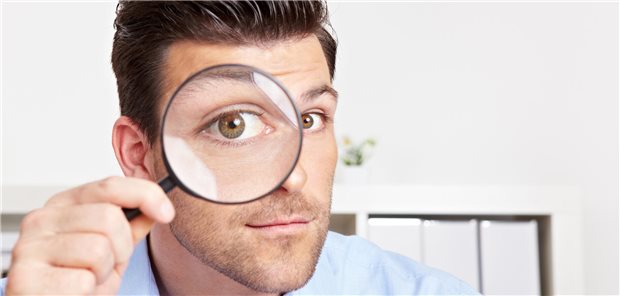 Ein Mann blickt durch eine Lupe.