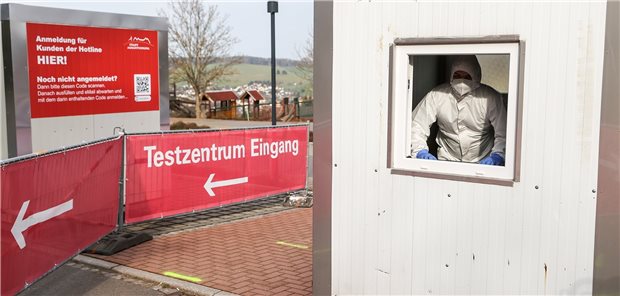 Neue Testverordnung drückt Kosten bei Coronatests deutlich Ein Mann in Schutzkleidung blickt aus dem Fenster eines Containers in einem Corona-Testcenter.