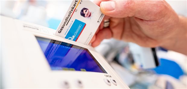 Ein Mitarbeiter einer Apotheke steckt eine Gesundheitskarte in ein Lesegerät.