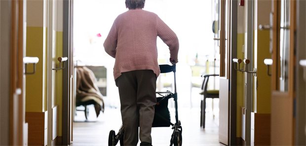 Eine Pflegeheimbewohnerin läuft mit einem Rollator durch ein Pflegeheim.