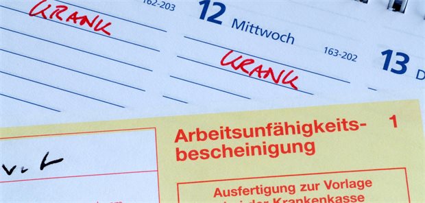 Eine AU liegt auf einem Kalender. Dort sind zwei Tage mit krank markiert.